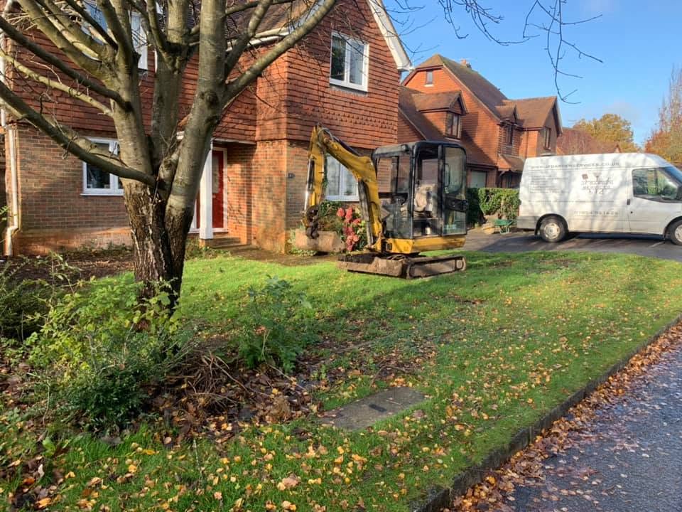 A mini digger at work on a front garden, with the JF van parked behind