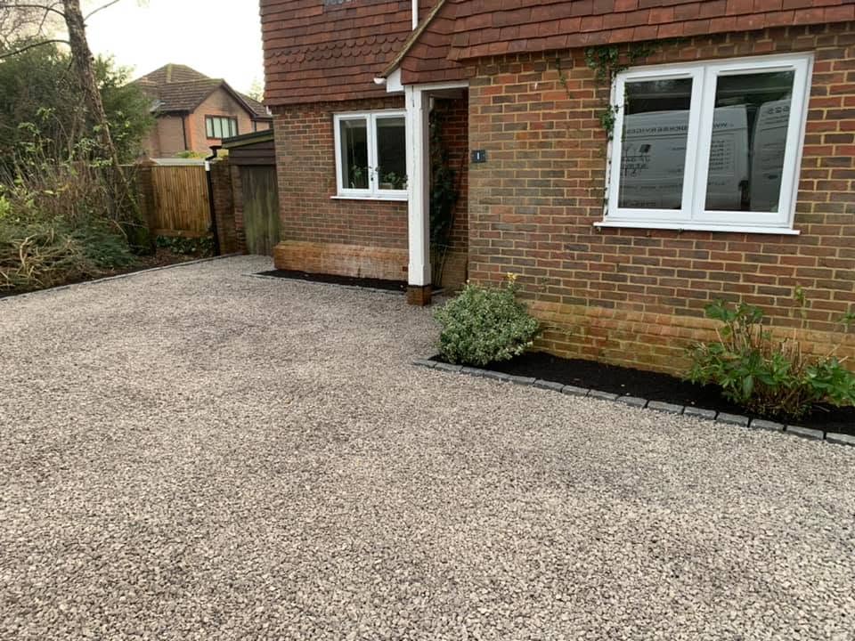 A finished gravel driveway beside a brick house with a newly planted border