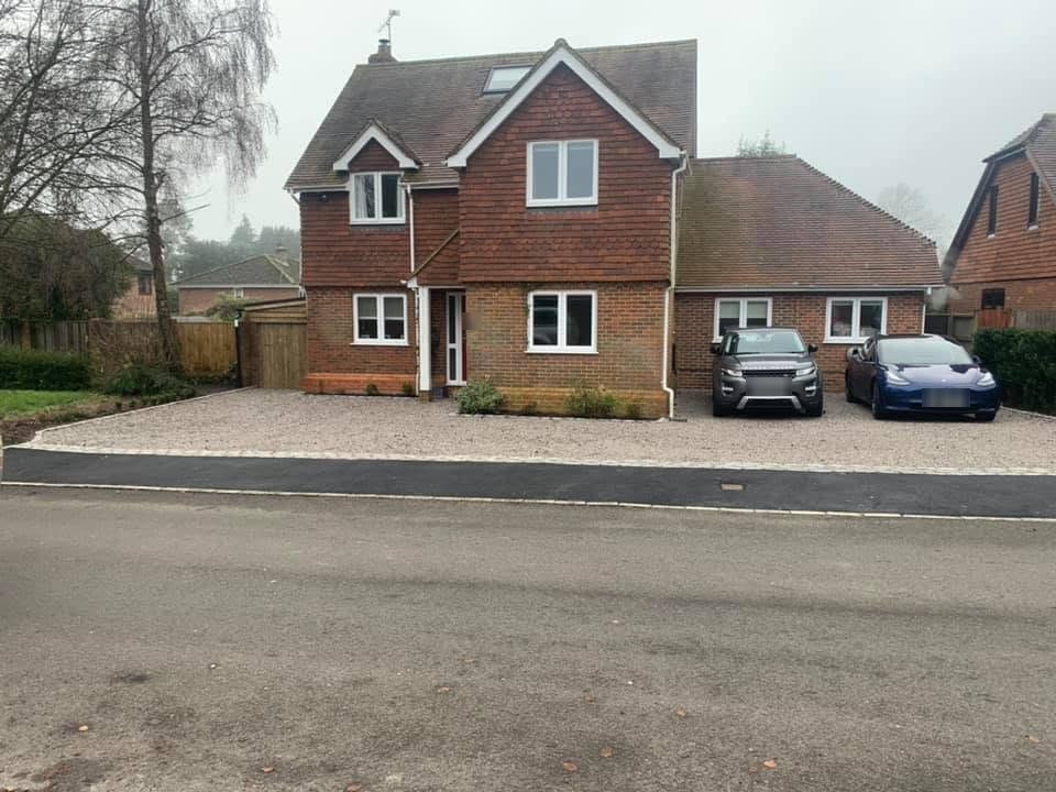 A wide finished gravel driveway in front of a detached brick house