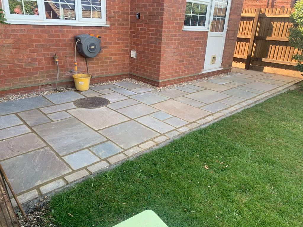 A new grey sandstone patio laid along a red-brick house wall beside a lawn