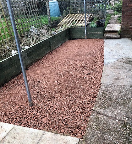 A narrow garden strip covered in red chippings, before the new lawn