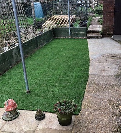 The finished artificial lawn filling the strip, with garden ornaments