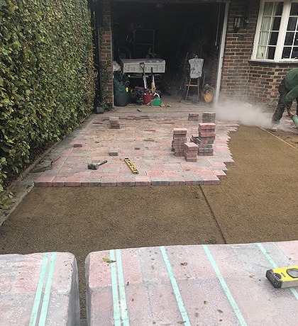 Block paving being laid in front of a garage, cut blocks stacked on the new bed
