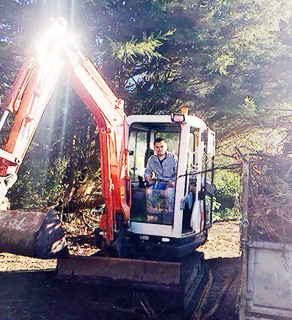 A mini digger working in a garden with the sun behind it