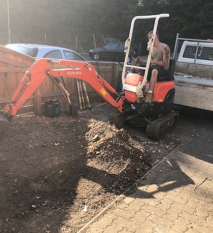 A small Kubota digger excavating beside a block-paved drive