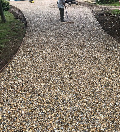 The curved drive with its gravel laid and edged, a man raking it level