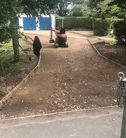 A mini digger cutting the line of a curved drive between two lawns