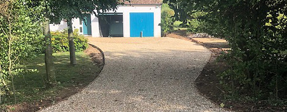 The finished curved gravel drive between trees, leading to a pair of blue garage doors