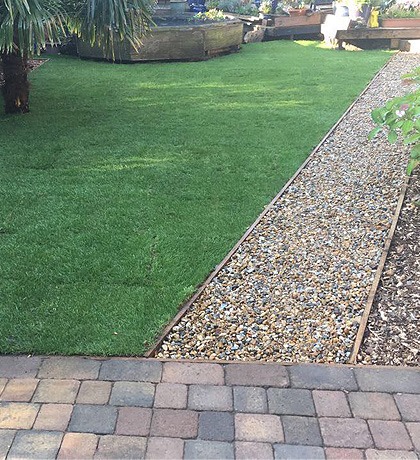A straight new lawn edged with gravel above block paving