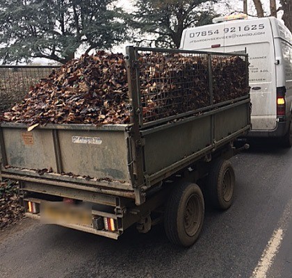 A caged trailer heaped with autumn leaves behind the JF Garden Services van