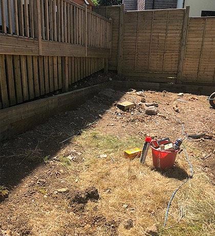 A bare, weedy corner of garden inside new fencing, before work starts
