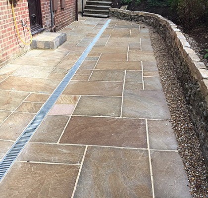 A new sandstone patio with a drainage channel running beside a dry stone wall
