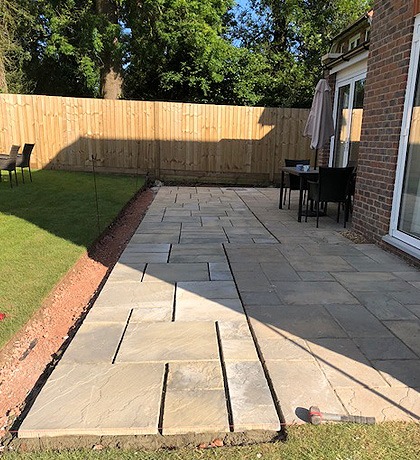 A sandstone patio running along the back of a house beside a new lawn edge