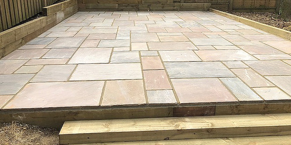 A wide finished sandstone patio with a timber step along its front edge