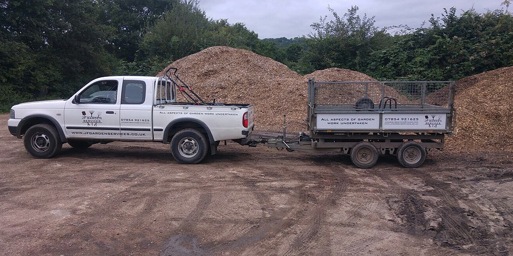 The JF Garden Services pickup and trailer beside heaps of wood chip