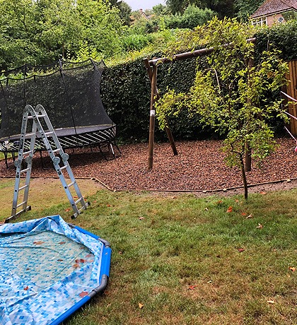 A garden play area with a swing, trampoline and new bark