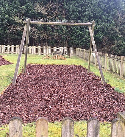 A swing frame standing in a fresh bed of play bark behind a picket fence