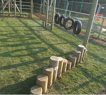 Turf and a row of log stepping posts under a tyre swing