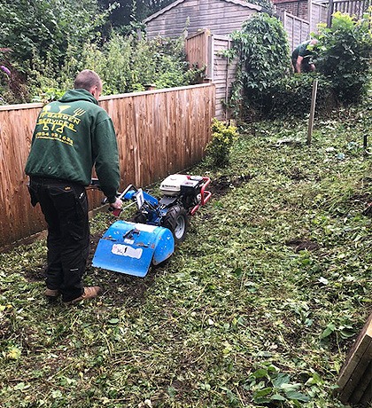 One of the team in a green JF Garden Services hoodie scarifying a lawn