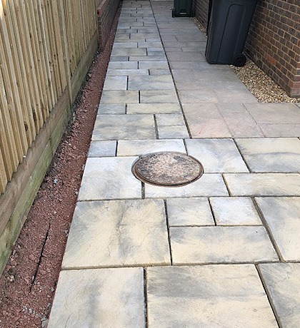 A narrow side path laid in grey paving slabs beside a fence
