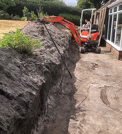 A mini digger cutting back a bank beside a house for a retaining wall