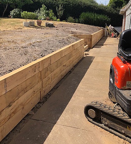 A new sleeper retaining wall along a concrete path, the digger beside it