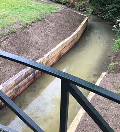The stream bank lined with new sleepers, seen from a footbridge